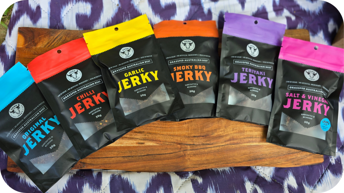 A colourful collection of 3099 Jerky bags in various flavors is displayed on a wooden board resting