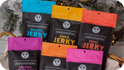 Colourful packs of 3099 Jerky in Garlic, Chilli, Teriyaki, and Original flavours displayed in a basket.