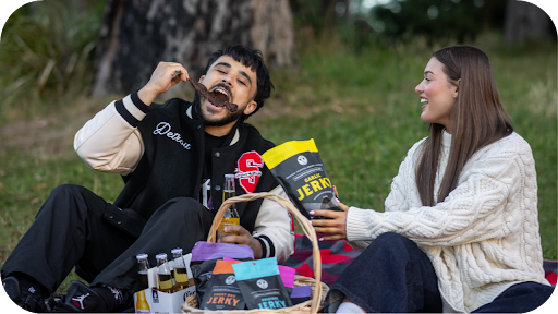 Couple enjoying beef jerky at a picnic in Australia with drinks and snacks, showcasing the fun of buying jerky online.
