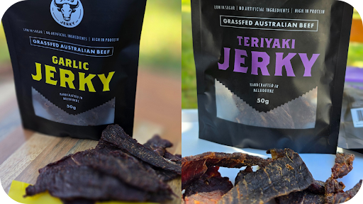 Garlic Beef Jerky pack with seasoned strips on wood beside Teriyaki Beef Jerky pack with tender slices, showcasing Aussie grass-fed handcrafted snacks side by side