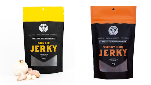 A side-by-side product shot of a yellow-topped bag of Garlic Jerky next to a bulb of garlic, and an orange-topped bag of Smoky BBQ Jerky.