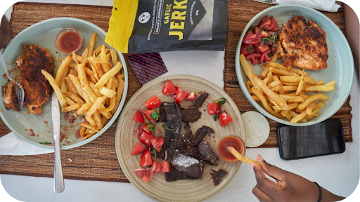  top-down view of three plates of food, including steak and fries, grilled chicken, and a central plate of chopped beef jerky with tomatoes.