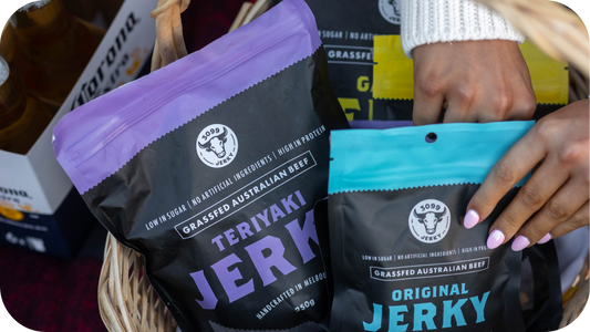 Close-up of a picnic basket filled with 3099 Jerky packs, including Teriyaki and Original flavours, with a hand reaching inside.