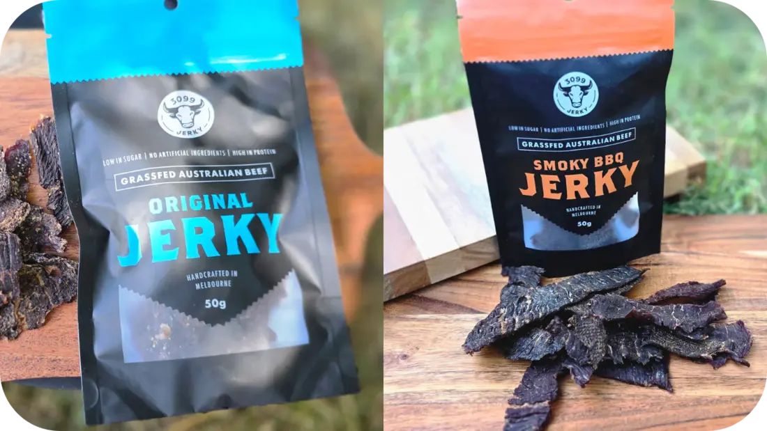 Two packs of 3099 Jerky, one Original beef jerky and one Smoky BBQ jerky, with strips of jerky on wooden boards outdoors in natural light