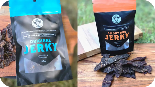 Two packs of 3099 Jerky, one Original beef jerky and one Smoky BBQ jerky, with strips of jerky on wooden boards outdoors in natural light