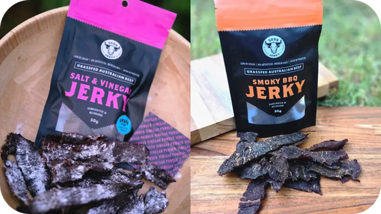 Salt &amp; Vinegar Jerky in a pink pack with seasoned slices on a wooden bowl beside Smoky BBQ Jerky in an orange pack with rich dark beef jerky strips